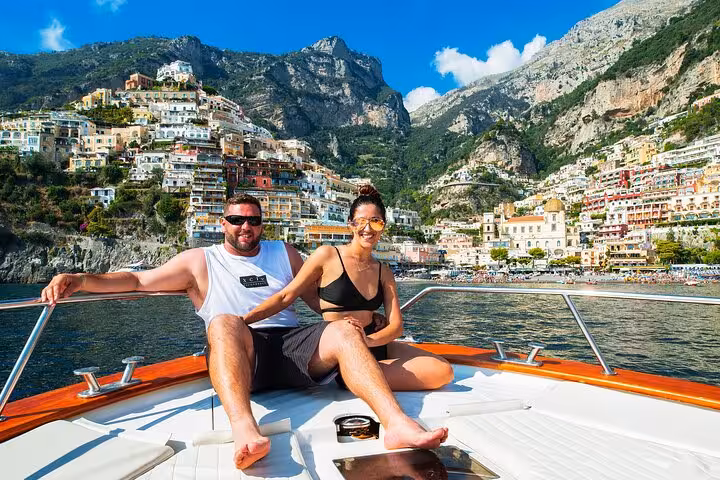 Smiling couple relaxing on a private boat tour with a stunning view of Positano's colorful cliffside buildings.
