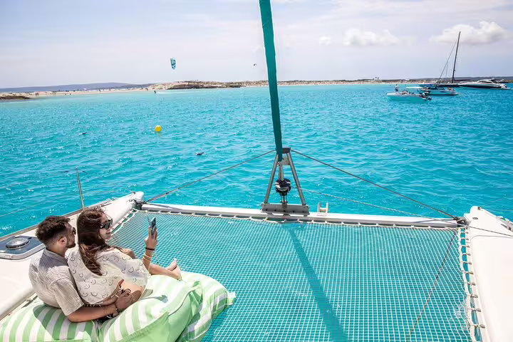 Couple relaxing on a private catamaran netting, enjoying stunning turquoise waters during a full-day Ibiza and Formentera trip.