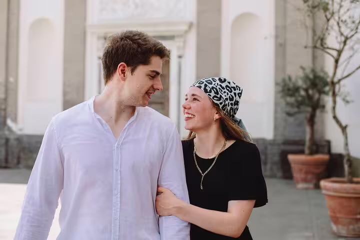 Happy couple walking arm in arm in front of a historic building in Naples, enjoying a private photoshoot experience.