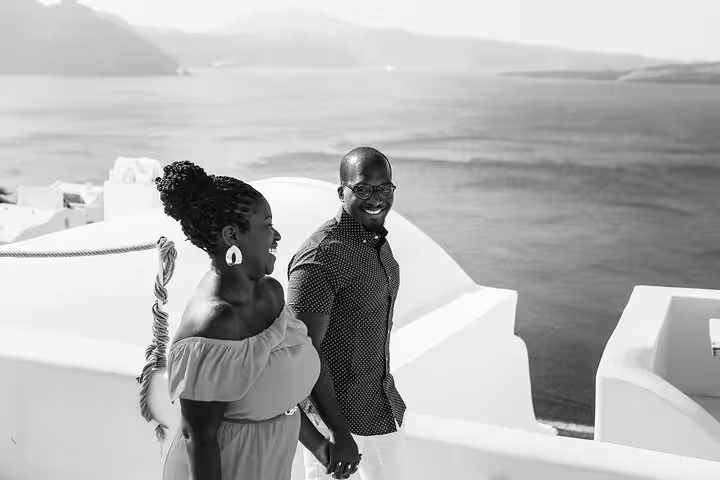 Couple walking on Santorini whitewashed terraces above the caldera, candid engagement moment with proposal photographer