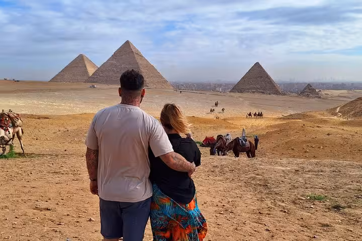 Couple embracing while overlooking the majestic Pyramids of Giza with camels and desertscape on a private tour.