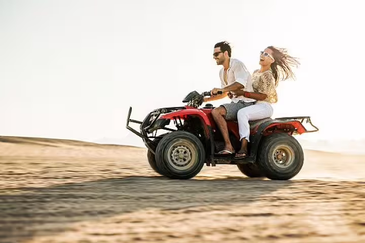 Couple on red quad bike speeding over desert dunes on a private ATV quad safari adventure from Sharm El Sheikh