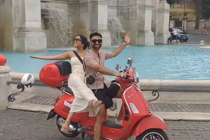 Smiling pair on a red Vespa in front of a beautiful fountain, capturing the essence of a Rome Vespa tour.