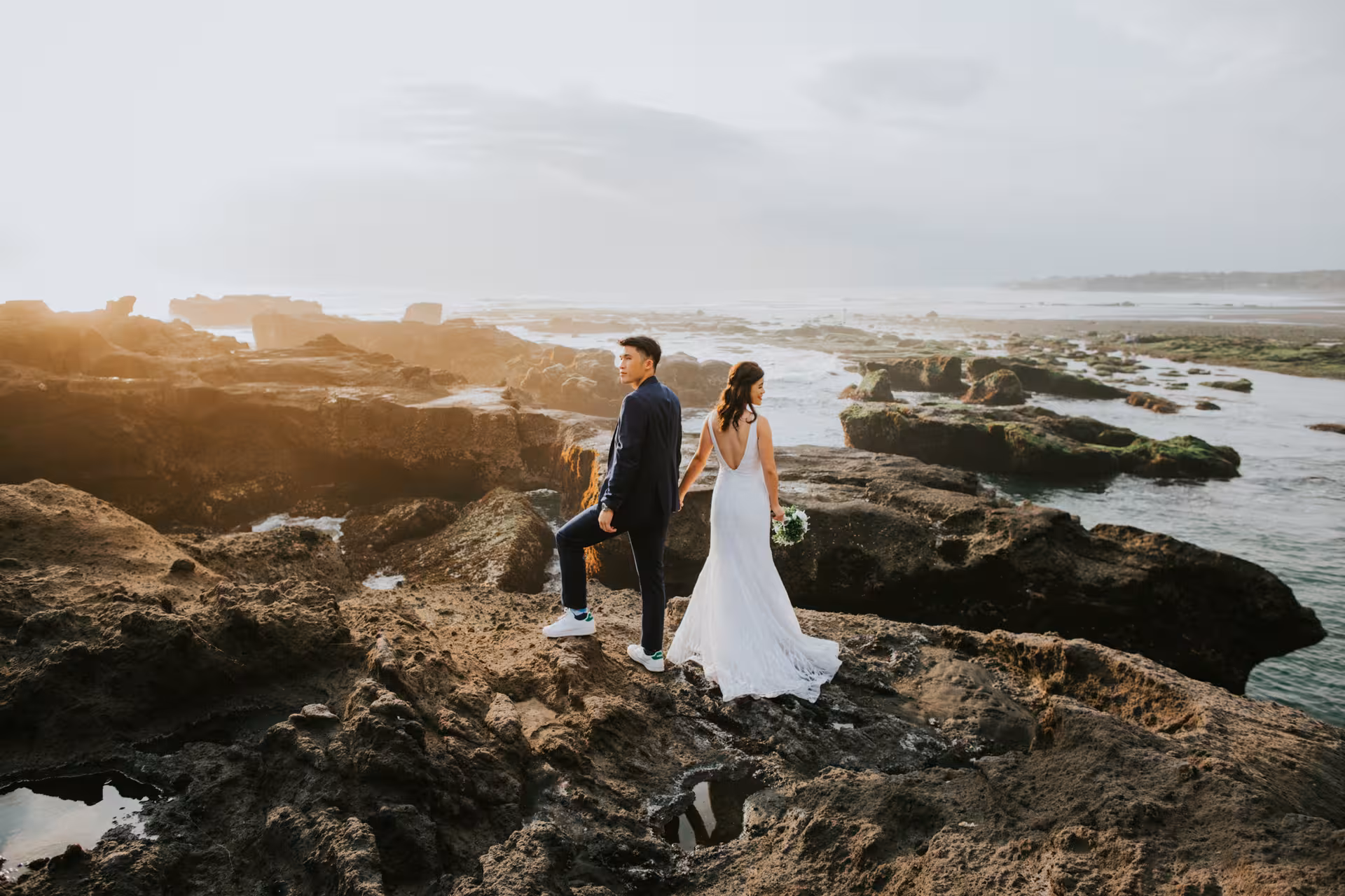Couple on rocky Bali coast with ocean view, capturing love and natural beauty in a professional photoshoot.
