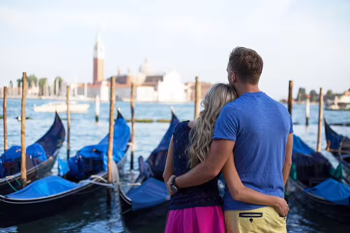 Couple embracing by moored gondolas on the Grand Canal in Venice, enjoying a romantic private gondola ride view at sunset