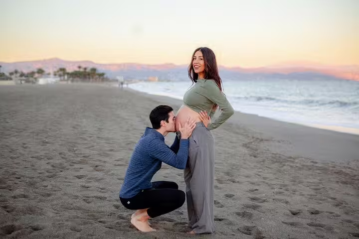 Couple enjoying a romantic maternity photoshoot on Marbella beach at sunset with a professional photographer.
