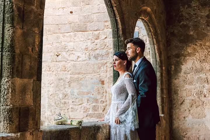 Couple in elegant attire gazing out from a stone archway in Rhodes, captured in a romantic photoshoot setting.