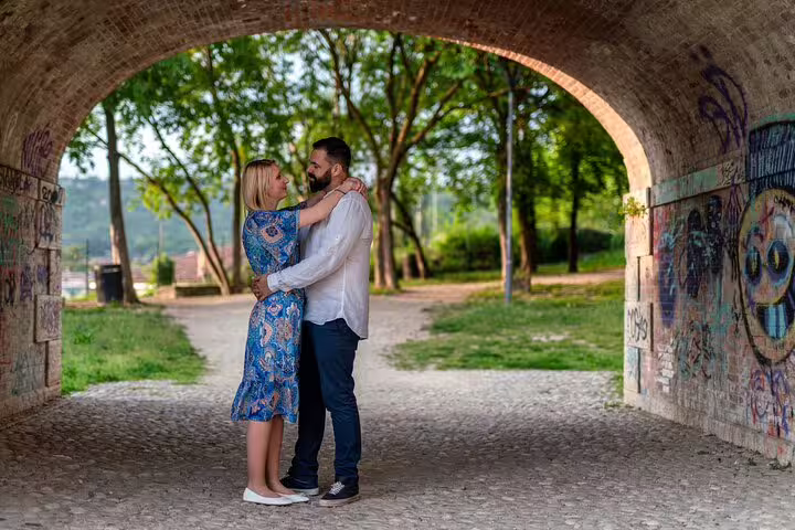 Couple embraces under a graffiti-decorated archway in a scenic park in Verona, capturing a romantic photoshoot moment.
