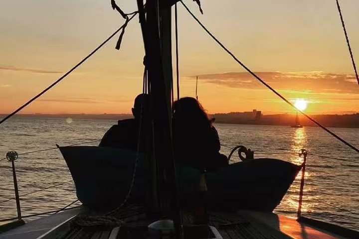 Couple enjoying a romantic sunset sailing tour on the Tagus River, silhouetted against a golden sky.