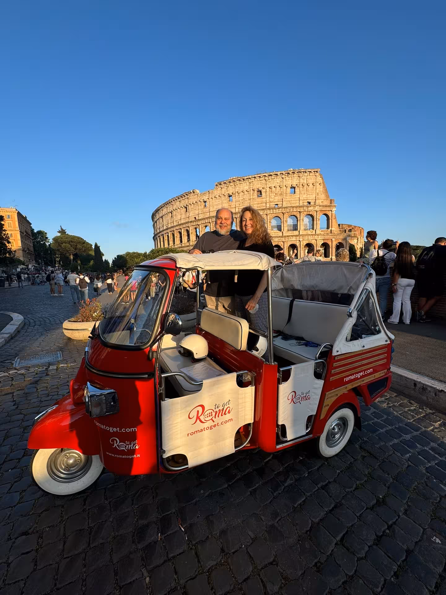Couple enjoying a scenic tour of Rome's Colosseum in a vintage red Piaggio ape calessino.