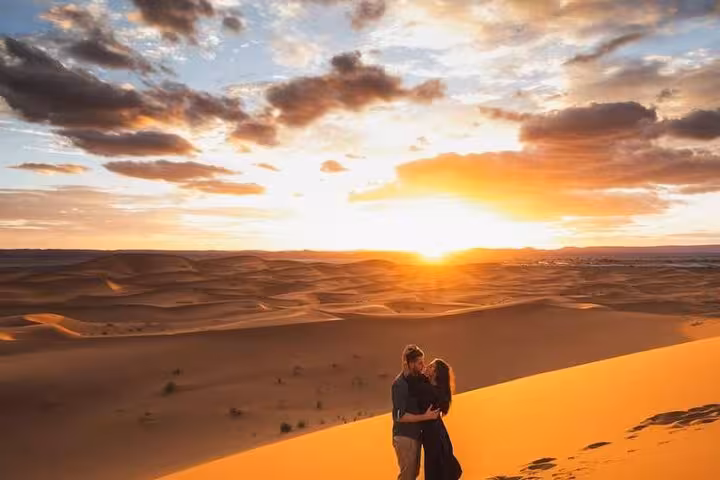Couple enjoying a romantic sunset view over the Sahara Desert dunes on a 3-day tour from Marrakech to Fes.