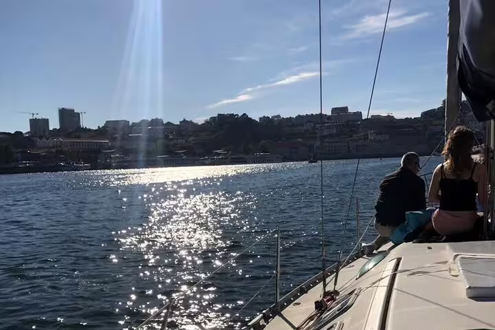 Couple relaxing on a sailboat deck with sparkling water and scenic Porto city backdrop, ideal for sunset cruises.