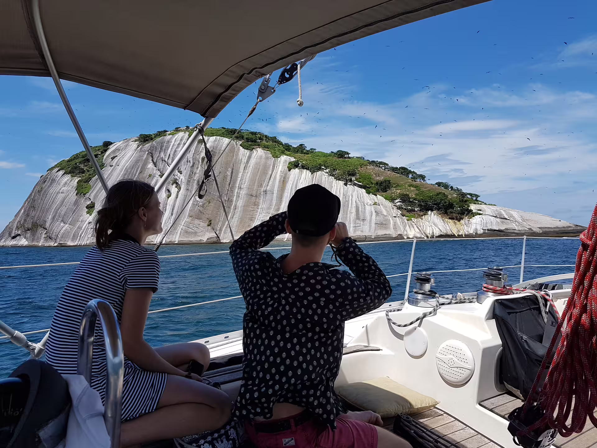 Couple on a sailboat admiring rocky island scenery during the Private Sailing Tour KAMEHAMEHA under a sunny sky.