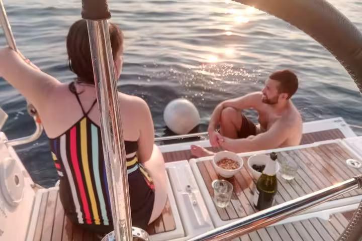 Couple relaxing on a sailboat at sunset in Barcelona, enjoying open bar drinks and snacks on deck
