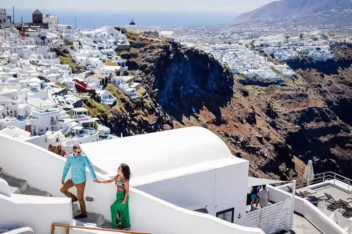 Couple walking Santorini cliffside in Oia, captured by proposal photographer with caldera views