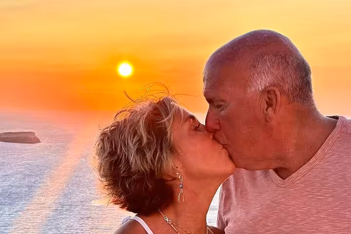 Couple kissing at Santorini sunset caldera viewpoint, romantic wine tour with tapas and winery stops