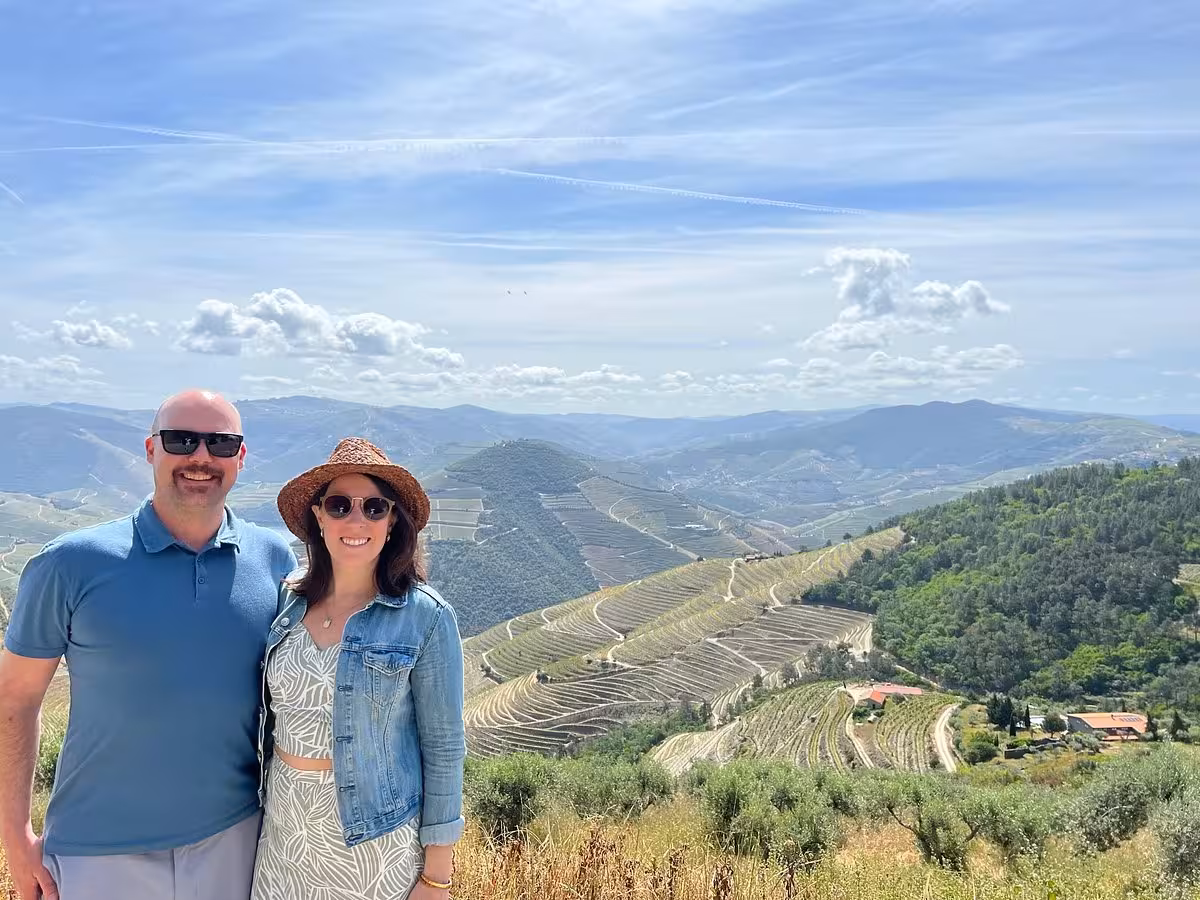 Couple at scenic viewpoint on panoramic tour, overlooking terraced vineyards and rolling mountain valley landscape