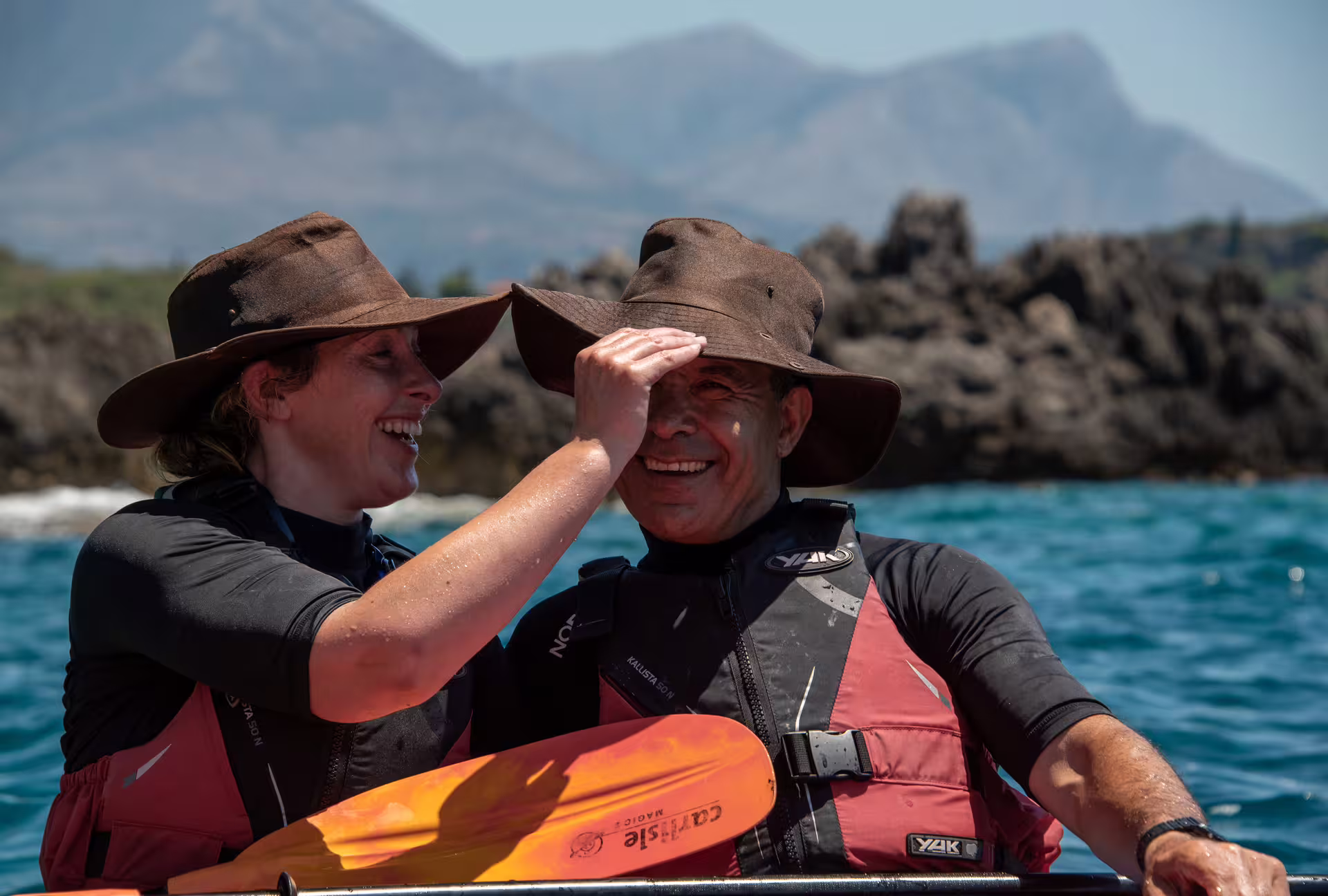 Couple smiling on a sea kayak tour in Kalamata, Messinia, wearing life vests by rocky coast and blue sea