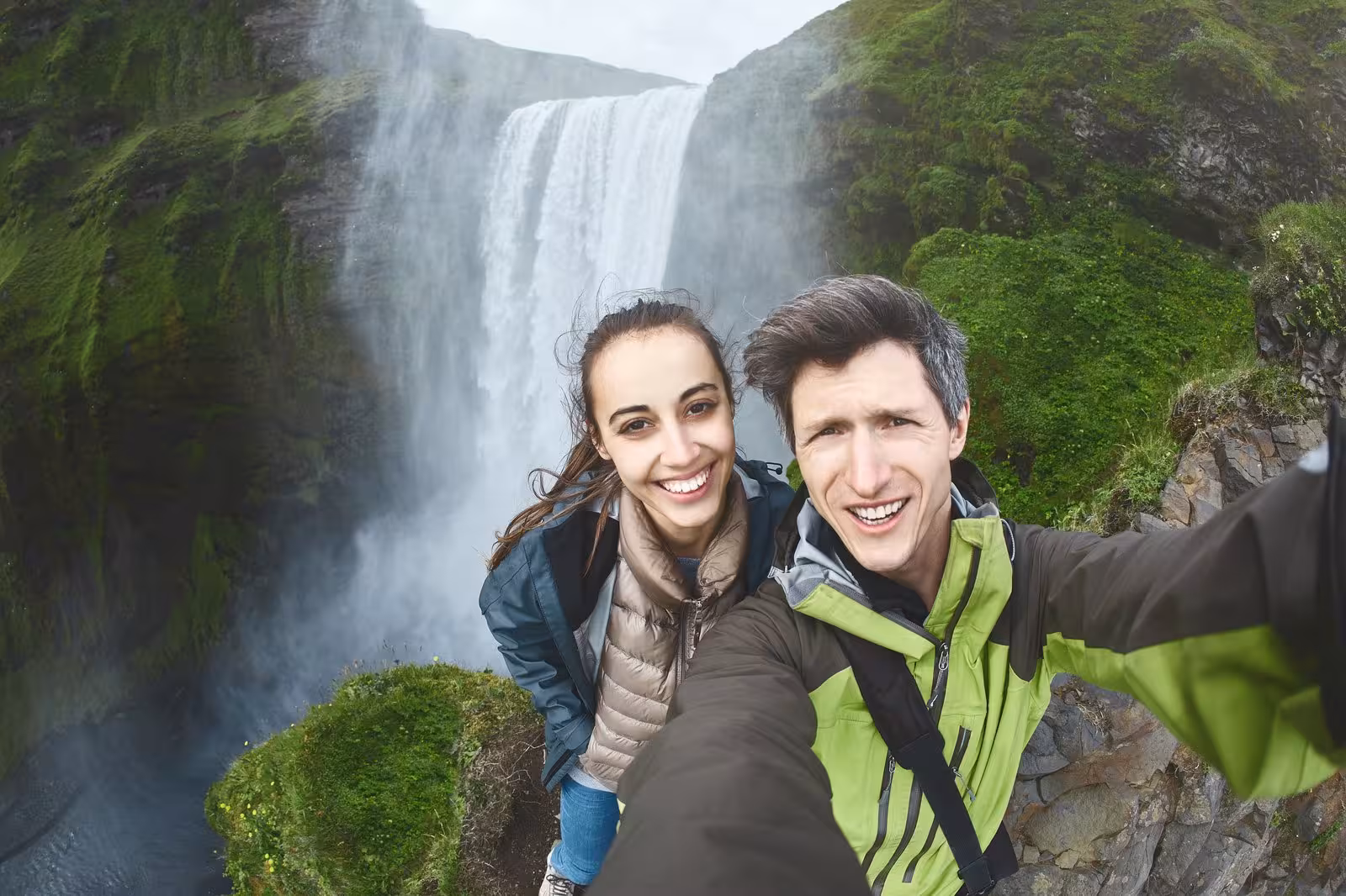 Couple taking a selfie at Skógafoss waterfall during a South Iceland self-drive adventure.