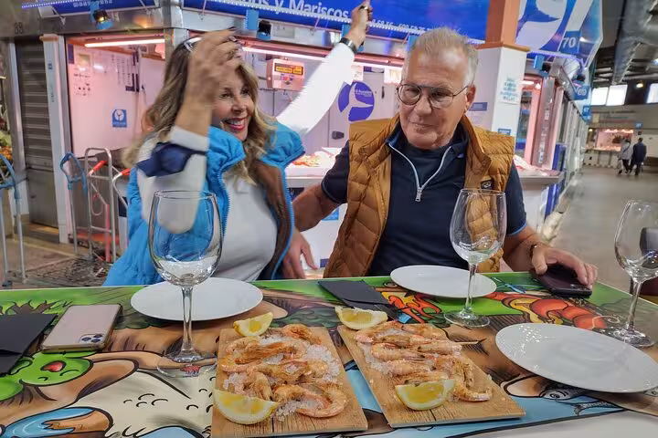 Couple savoring fresh shrimp and wine at a vibrant market stall on the Taste of Marbella Food & Market Tour.