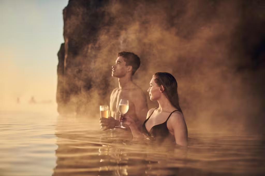 Couple enjoying drinks in the steamy waters of Sky Lagoon, Iceland, showcasing relaxation after Silfra snorkeling adventure.