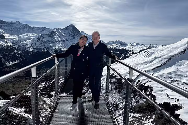 Couple smiles on a snowy mountain viewing platform during a private day trip to Grindelwald in the Swiss Alps.