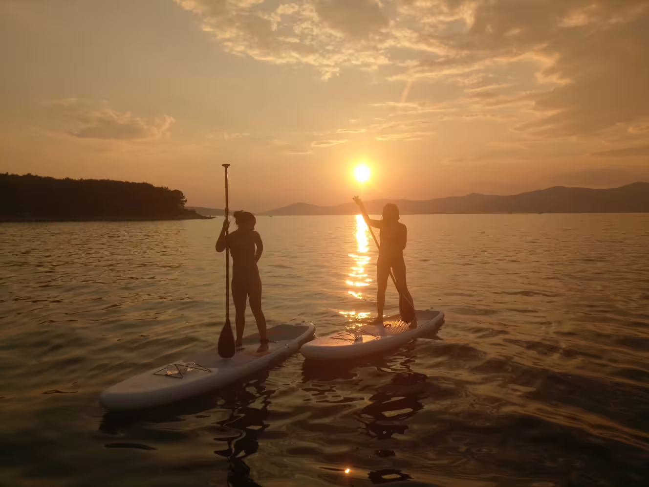 Couple stand up paddleboarding at sunset near Split, Croatia, on an Adriatic SUP tour with wine tasting