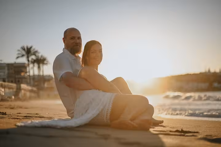 Couple sitting on a sandy beach at sunset, showcasing a romantic private photoshoot experience in Hersonissos.