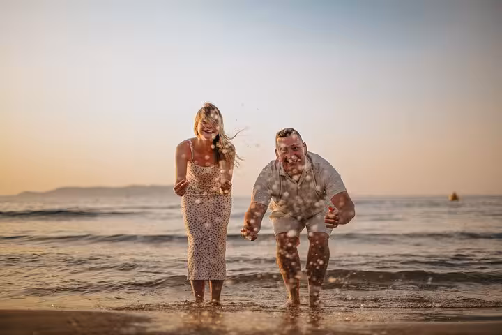 Couple laughing and splashing water on a Gouves beach at sunset, ideal for capturing joyful moments in a private photoshoot.