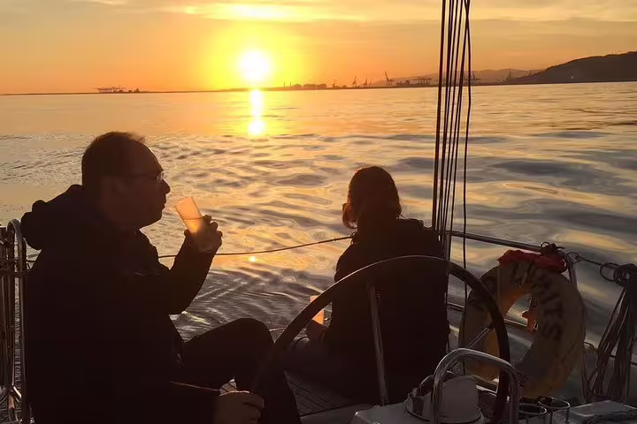 Couple enjoying drinks on a sailboat during a 2-hour exclusive sunset cruise from Barcelona, with vibrant sunset views.
