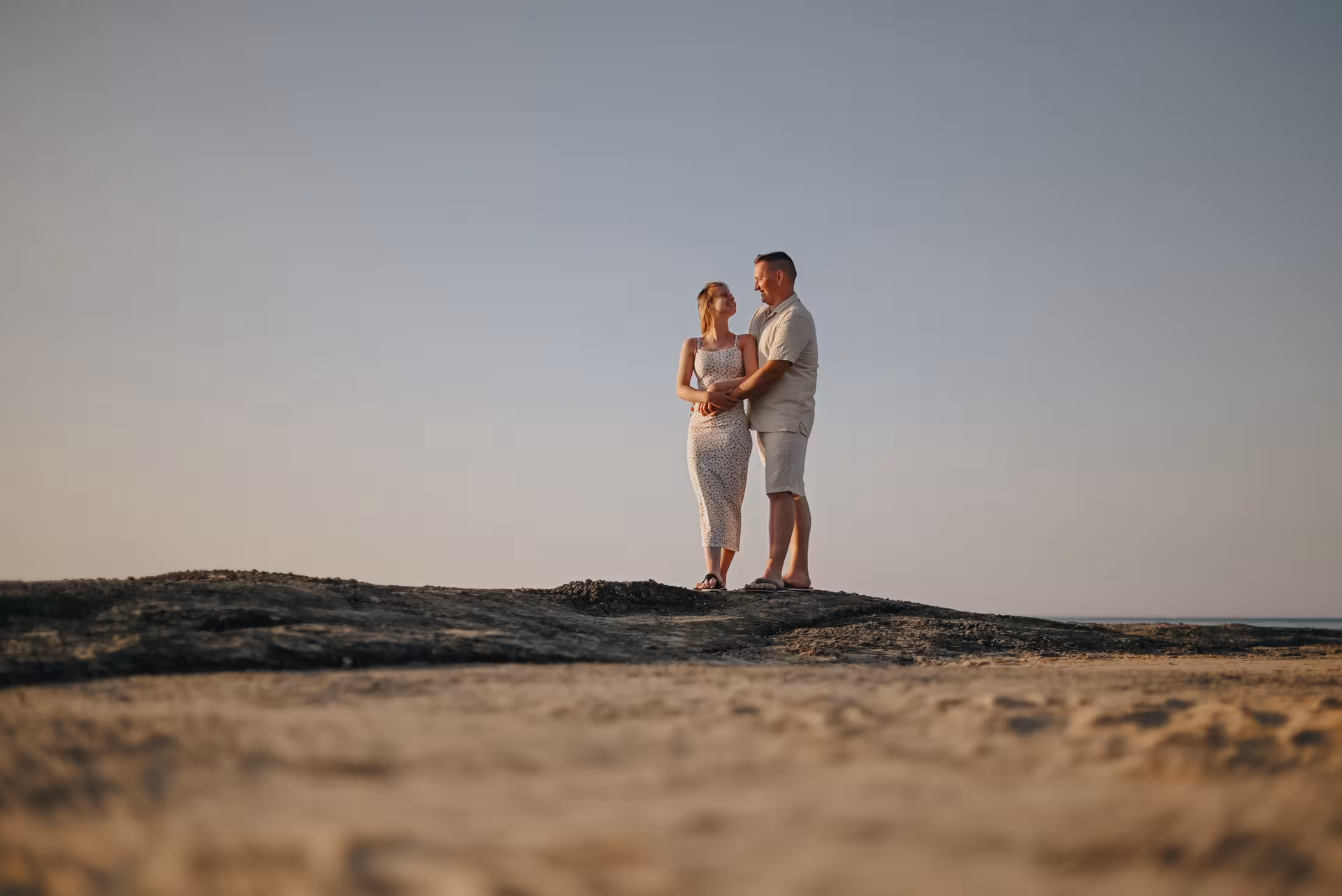 Couple embracing on a rock during a serene sunset photoshoot in Analipsi.