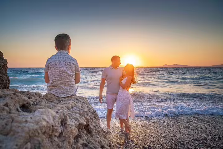 Couple embracing at sunset on a Rhodes beach with a child watching, captured during a professional photoshoot.
