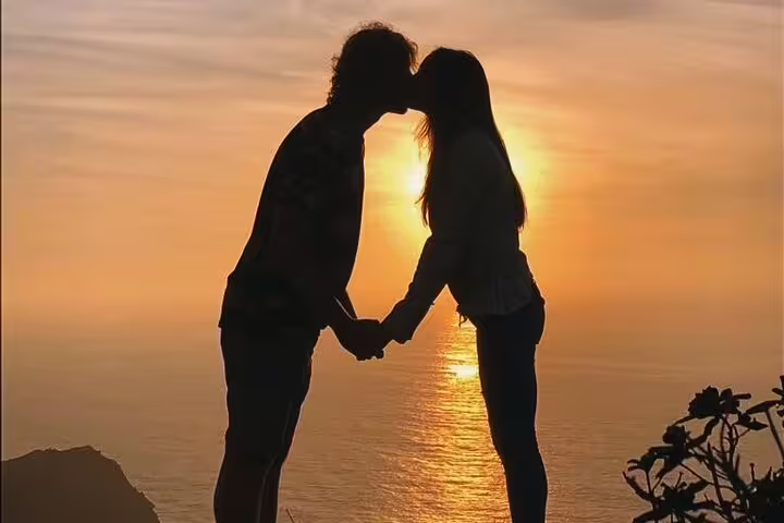 Romantic couple shares a kiss at sunset overlooking the ocean on the scenic West Coast 4x4 tour.