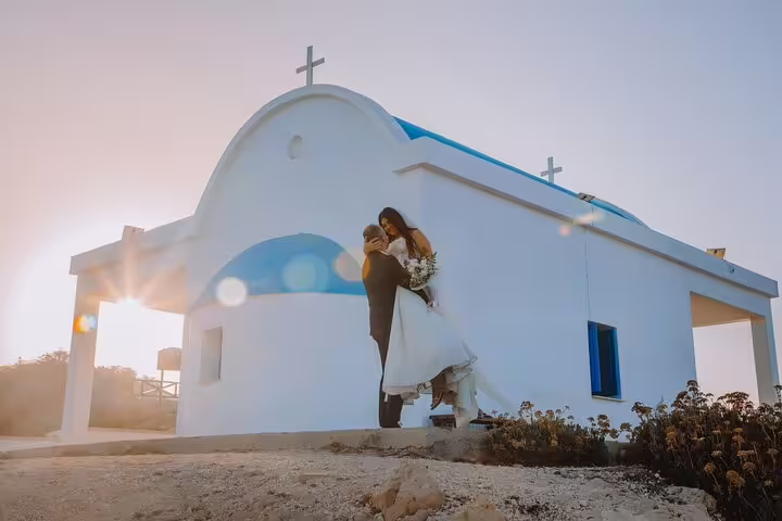 Couple posing romantically at sunset by a white chapel with blue dome in Ayia Napa during a private photoshoot.