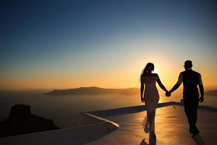 Couple holding hands at sunset on a Santorini rooftop, capturing romantic moments with a personal vacation photographer.