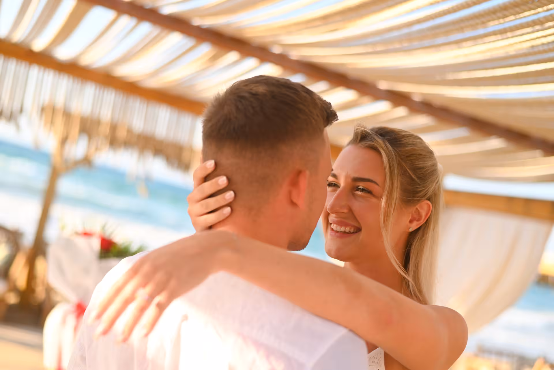 Couple embracing under a pergola by the sea at a surprise proposal in Heraklion Venetian Port.