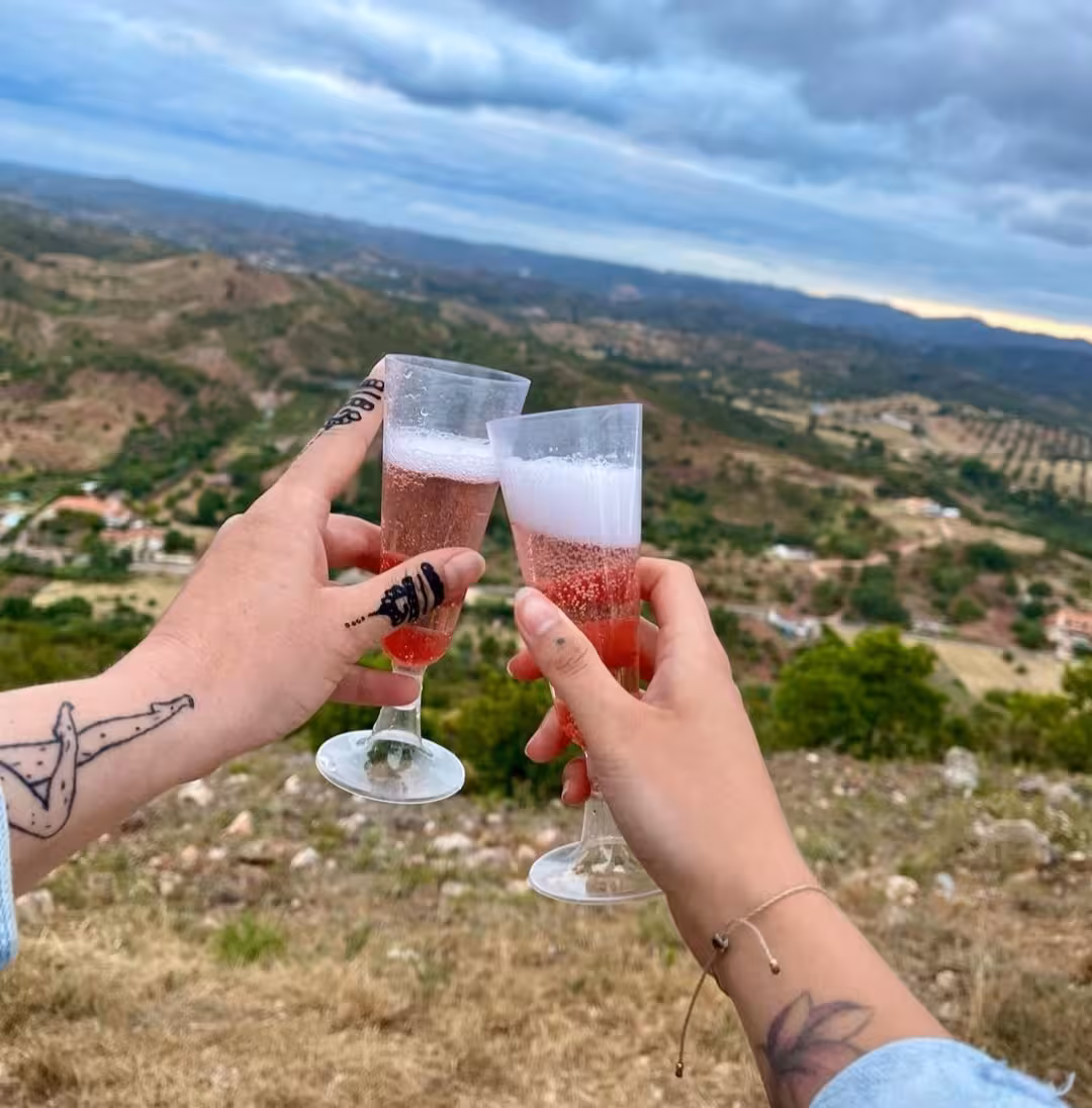 Couple toasting rosé sparkling wine at sunset viewpoint overlooking rolling green hills on a romantic countryside tour