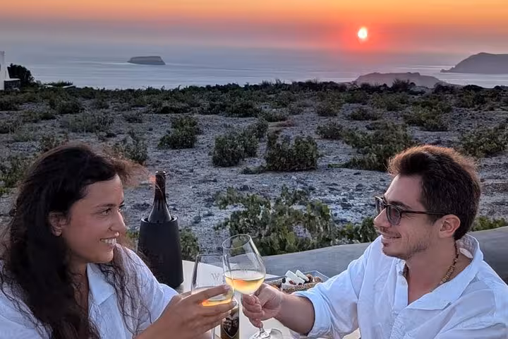 Couple toasting Santorini wine at sunset on a private honeymoon tour overlooking the caldera and Aegean Sea