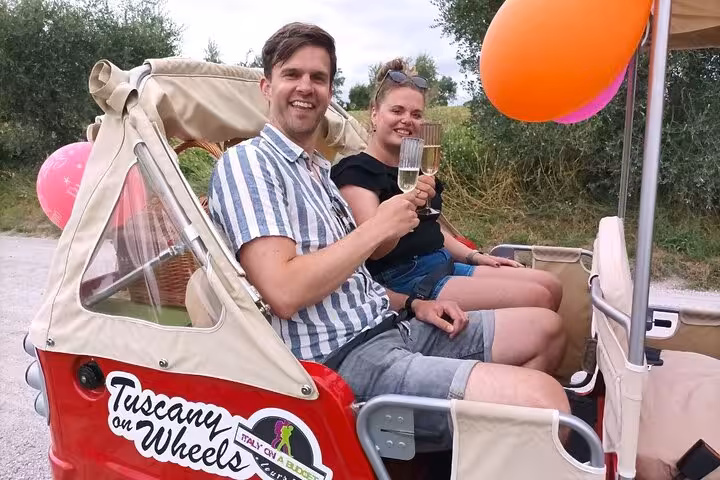 Couple toasting with wine glasses on a Tuscany tuk-tuk tour, celebrating a delightful day in the Italian countryside.