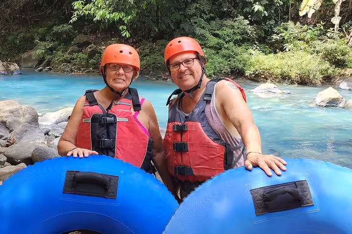 Couple smiling with inner tubes along the vibrant Celeste River, ready for an adventurous tubing experience in Costa Rica.