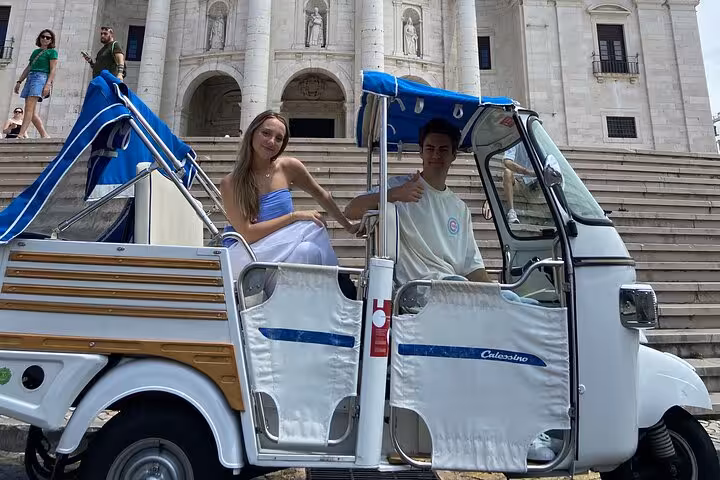 Couple posing in tuk-tuk by Lisbon Cathedral stairs, scenic city highlights tour paired with sunset sailboat cruise