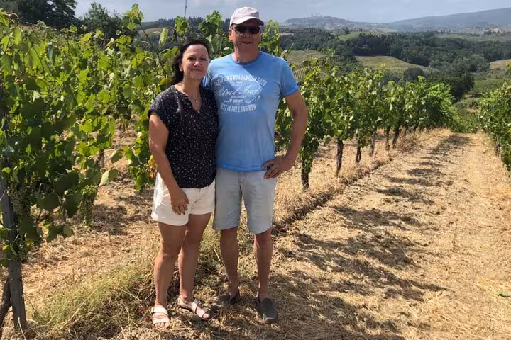 Couple enjoying a sunny day in a Tuscan vineyard, showcasing the lush greenery and scenic hills.