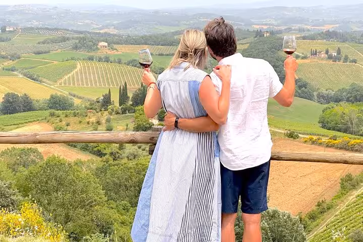 Couple enjoying a scenic view of Tuscany vineyards with wine glasses in hand during a Chianti tour.