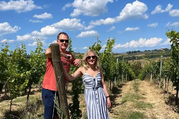 Couple enjoying a sunny day in a vineyard during a Tuscany wine tour, surrounded by lush grapevines and scenic hills.