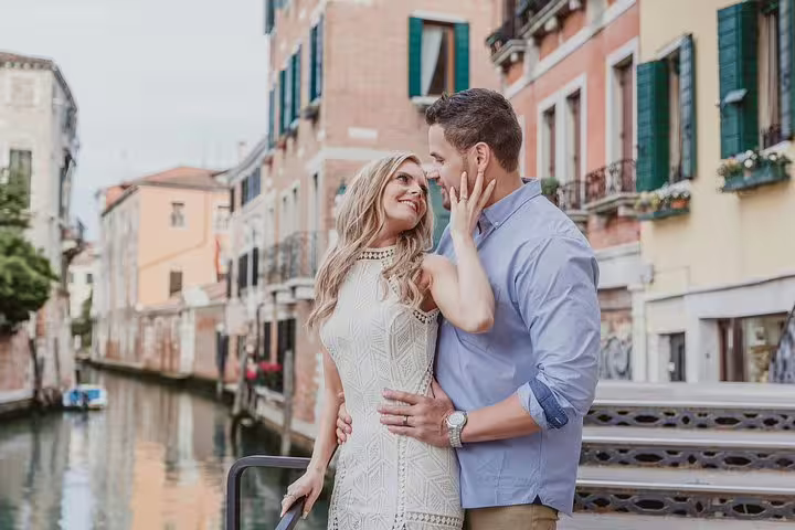 Happy couple sharing a moment on a picturesque bridge over a Venice canal, surrounded by colorful historic buildings.