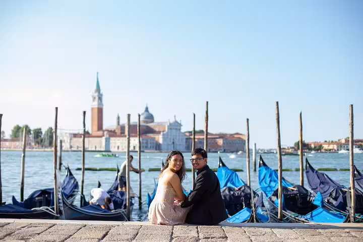 Couple seated by Venice gondolas with San Giorgio Maggiore view, destination wedding photography session