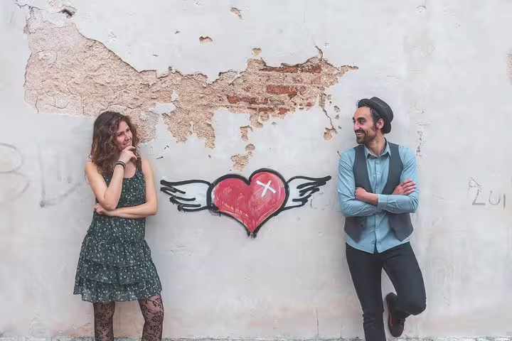 Couple posing by heart street art wall, playful city portrait session with professional photographer