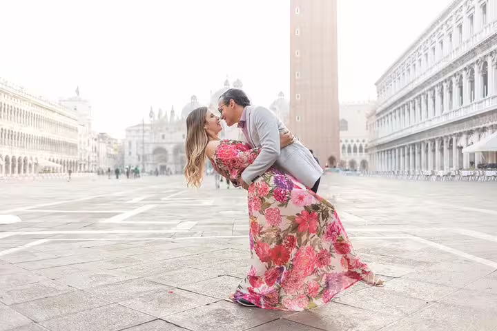 Couple kiss in St Mark’s Square during Venice city portrait photo session, floral dress and iconic campanile