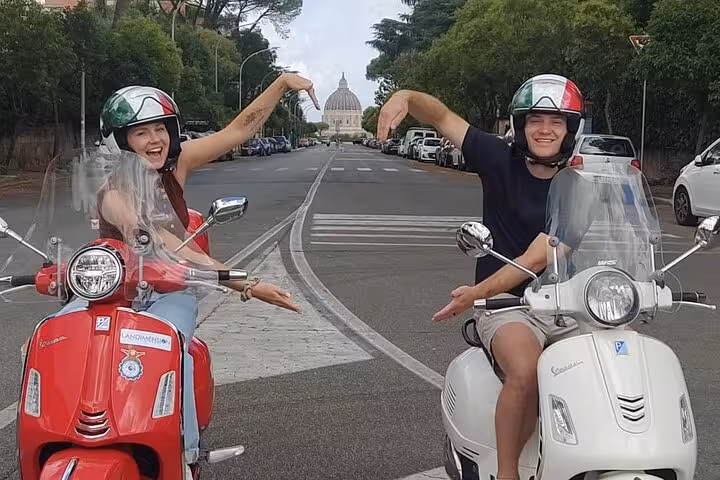 Couple on Vespas with St. Peter's Basilica in the background during a Rome Highlights by Vespa tour.