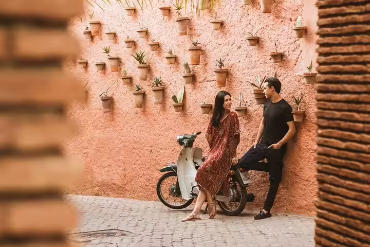 Couple posing by vintage scooter against a decorative wall during private photo shoot in Marrakesh, Egypt.